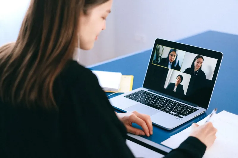 A woman at her desk on a video call, her laptop screen showing three other women.